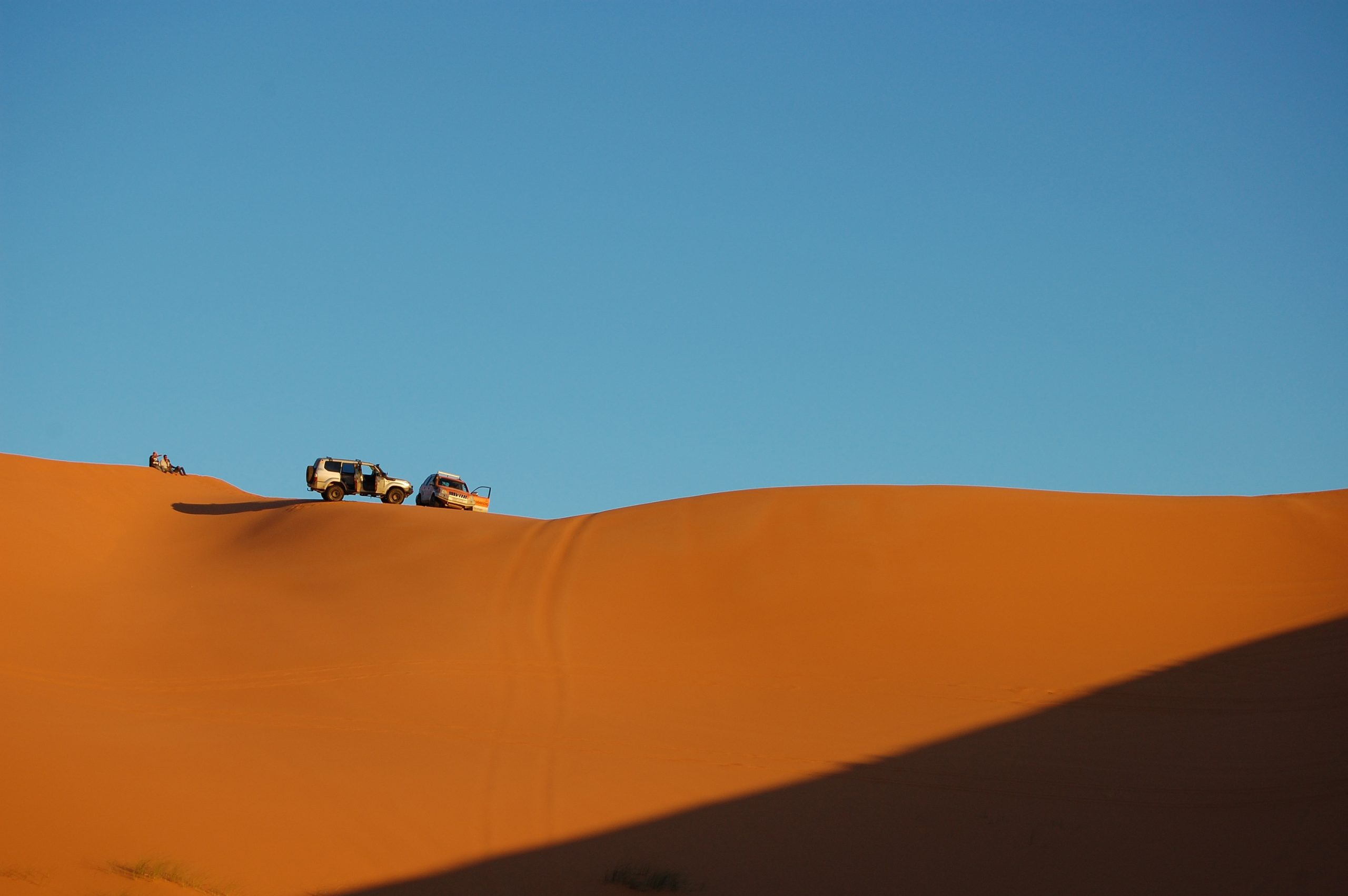 A long-range shot of two cars parked on top of the sand dunes with clear blue sky on a sunny day